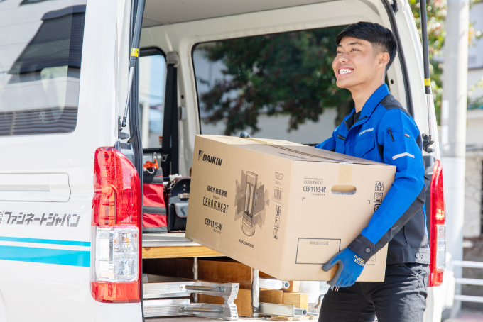 「ファシネートジャパン」の青い制服を着た男性が、社名入りの車両からダイキン製機器（セラムヒート）の梱包箱を運び出している様子
